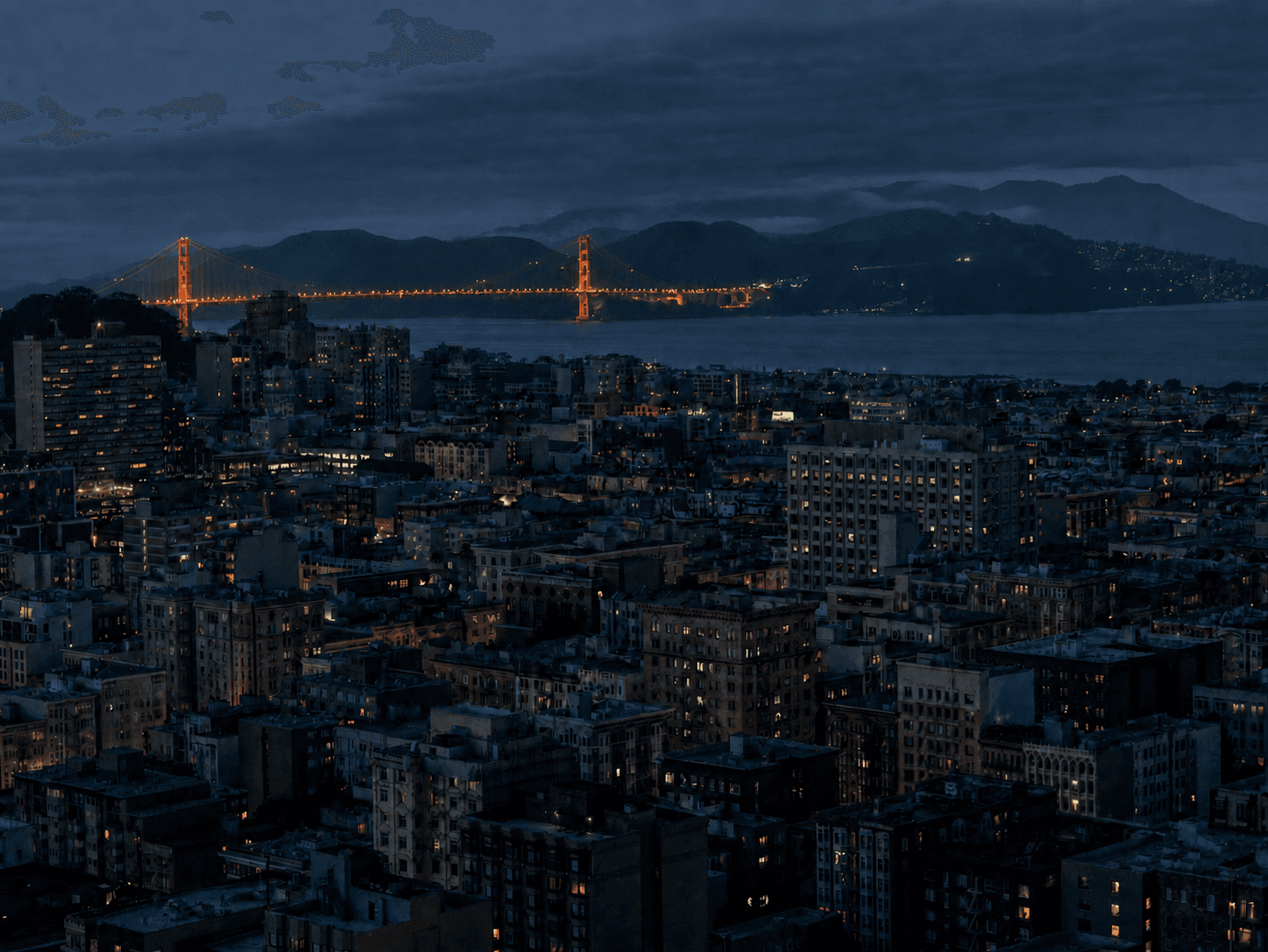 San Francisco Bay at night, with the Bay Bridge, a ferry, illuminated hills, and downtown beneath low clouds.